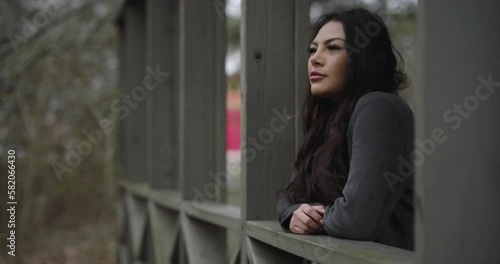 Young hispanic lady thinking on a bridge in small nature park. Thoughtful contemplative woman.