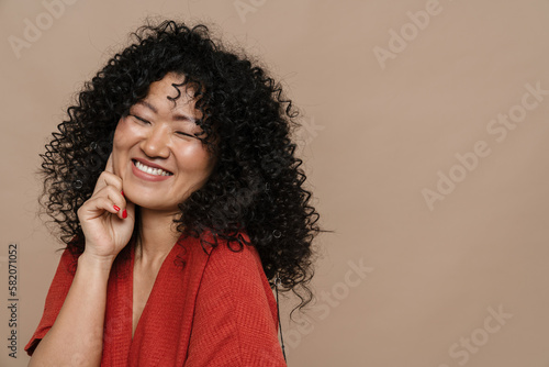 Cheerful asian woman posing while standing isolated over beige background