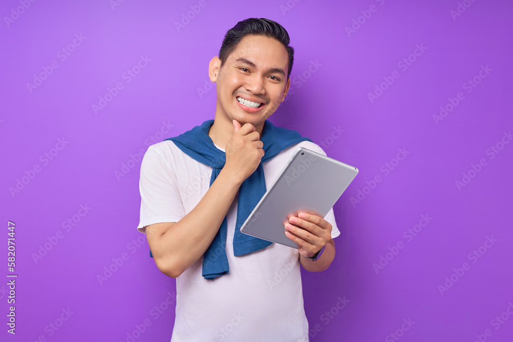 Portrait of smiling young Asian man in white t-shirt using digital tablet isolated on purple background Portrait of smiling young Asian man in white t-shirt using digital tablet isolated on purple background
