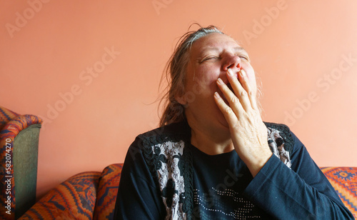 Sleepy elderly woman yawning on sofa at home.