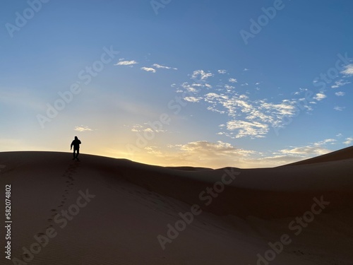 A silhouette of a man climbing a sand dune towards the sunrise Morocco 