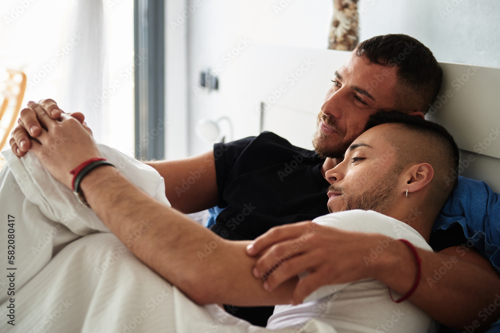 Male gay couple cuddling while relaxing in bed together. Male gay couple cuddling while relaxing in bed together.