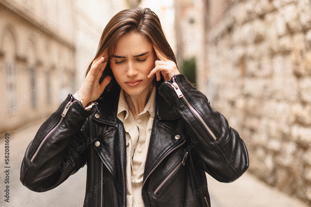 Fototapeta premium Panic attack on the street. Female touch her head with her hands as she stands in the street. Female feeling headache on the street. Stressed woman outside.