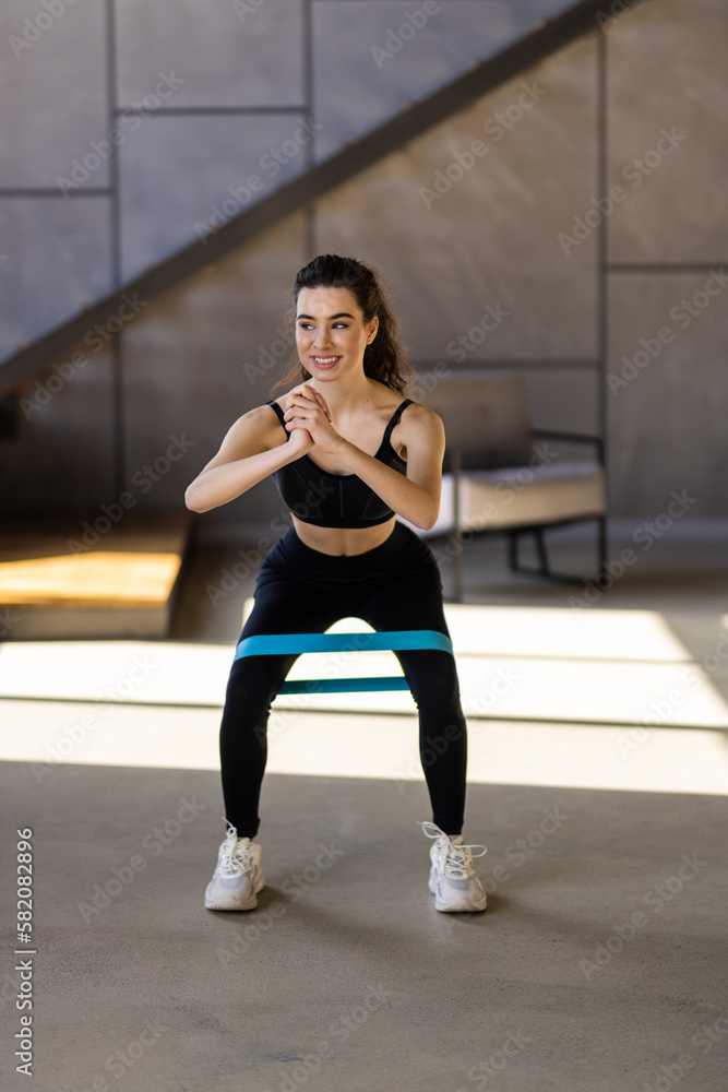 Fototapeta premium Young woman during her fitness workout at home with rubber resistance band