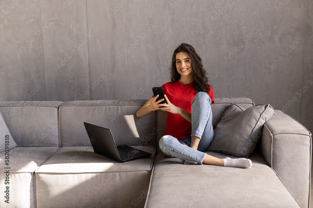 Excited young woman watching media content on line in a mobile phone sitting on a couch in the living room Excited young woman watching media content on line in a mobile phone sitting on a couch in the living room