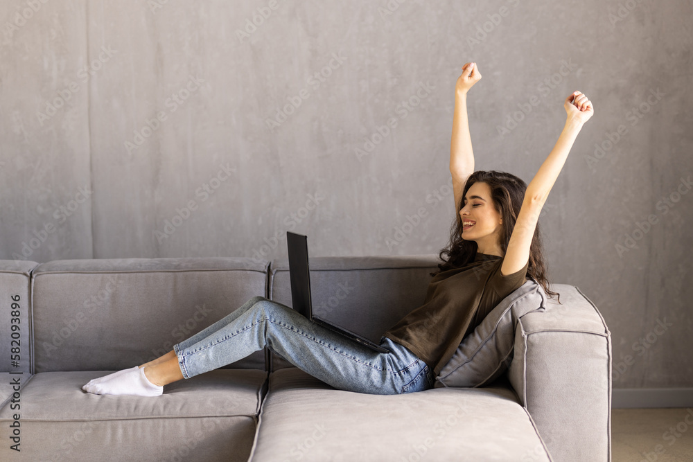 Woman sit on sofa put pc on lap clenched fists scream with joy while read great news on laptop. Gambler celebrate online auction bet victory. Woman sit on sofa put pc on lap clenched fists scream with joy while read great news on laptop. Gambler celebrate online auction bet victory.