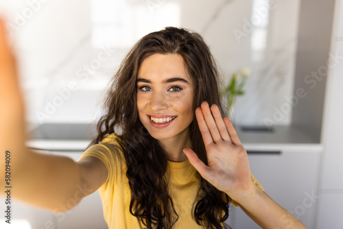 Young smiling beautiful positive ginger woman indoors at home take selfie by camera.