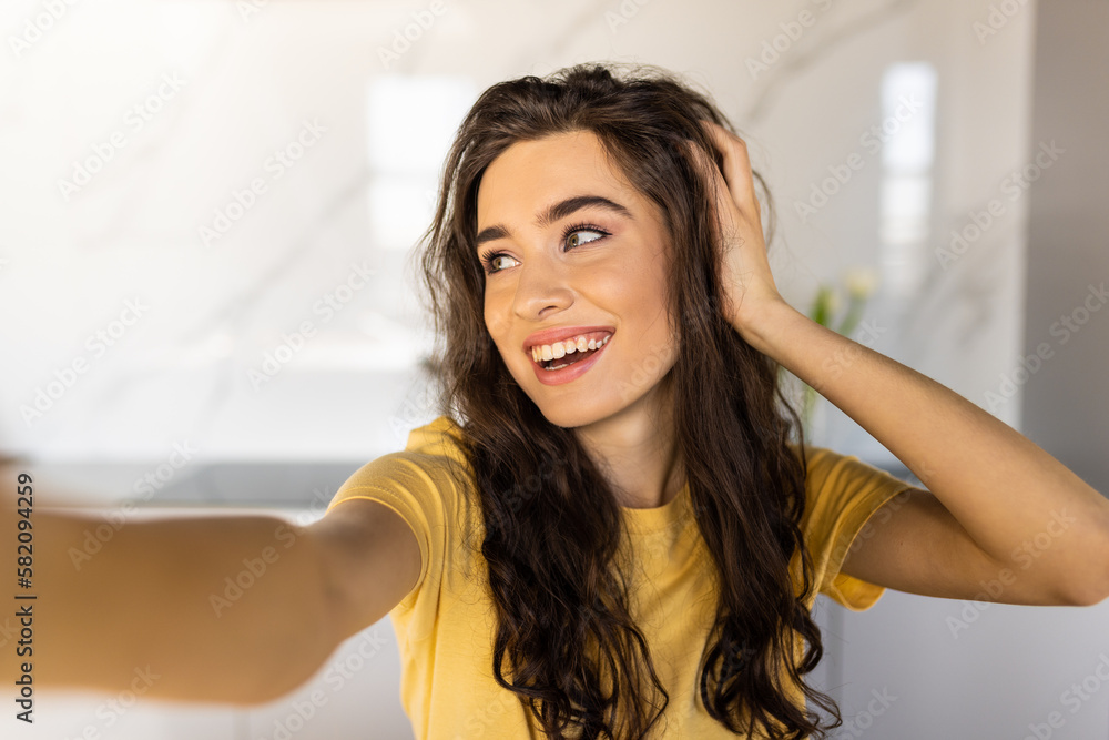 Cheerful young woman taking a selfie at the kitchen