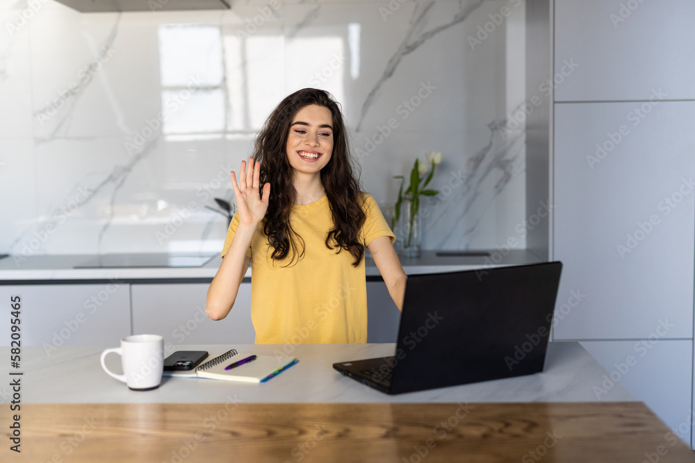 Young woman waving hands at the laptop and having video call with her friends while working from home Young woman waving hands at the laptop and having video call with her friends while working from home