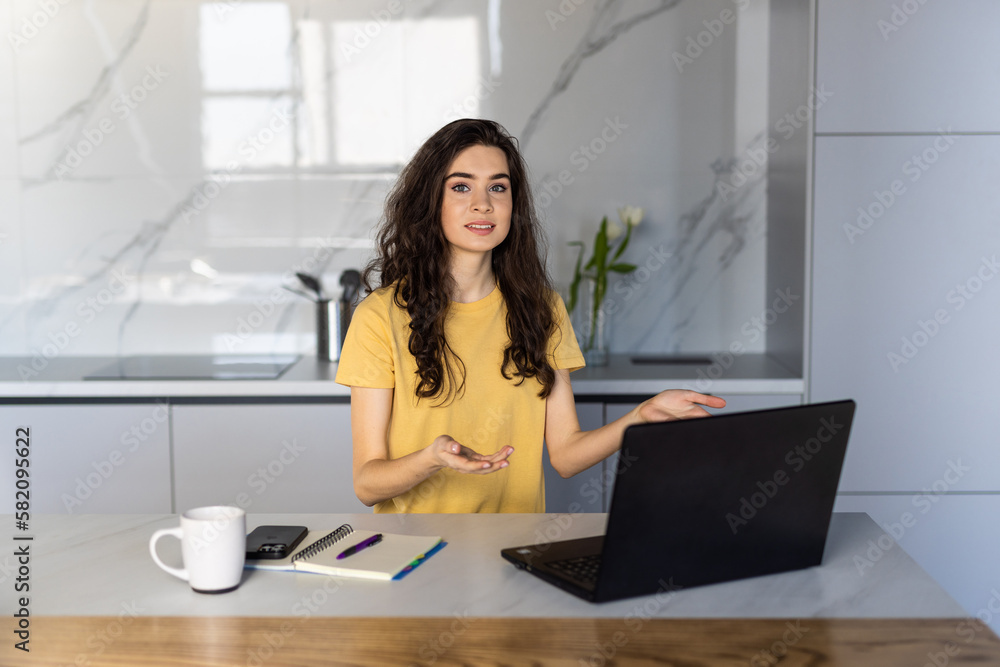 Smiling young woman making video call and heaving a breakfast in her kitchen. Smiling young woman making video call and heaving a breakfast in her kitchen.