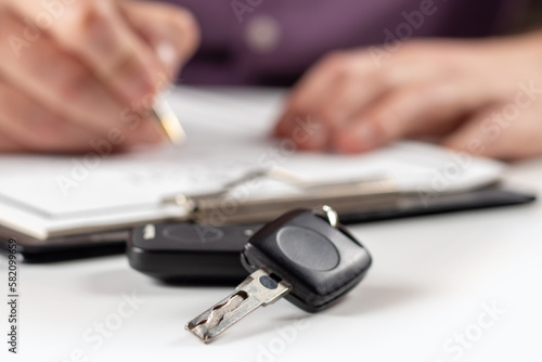 Car keys on desk with man signing purchase documents in background.