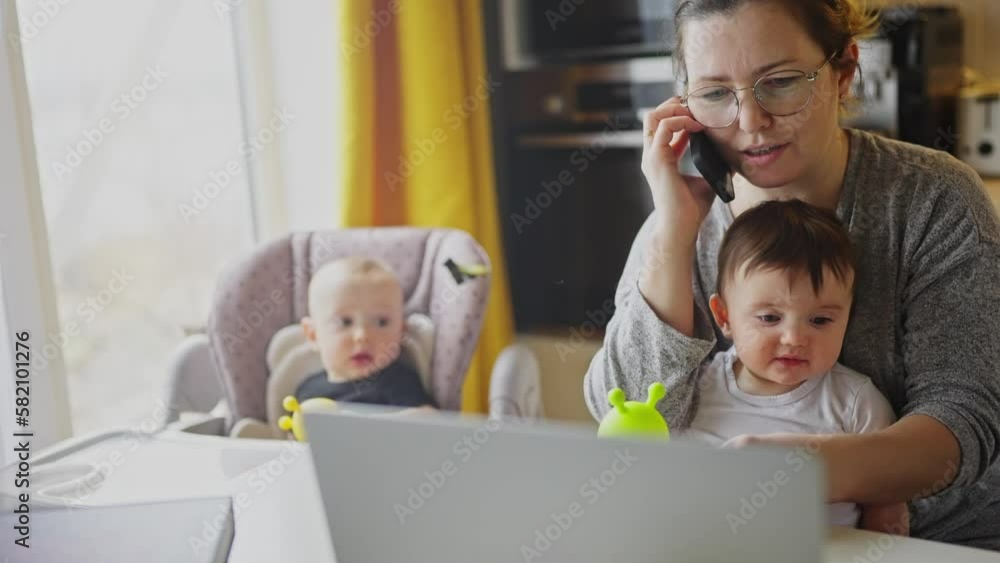 mother working from home remotely with baby daughter in his arms. pandemic remote work business a concept. mother tries to work at home in kitchen, fun baby children interfere sitting on their hands mother working from home remotely with baby daughter in his arms. pandemic remote work business a concept. mother tries to work at home in kitchen, fun baby children interfere sitting on their hands