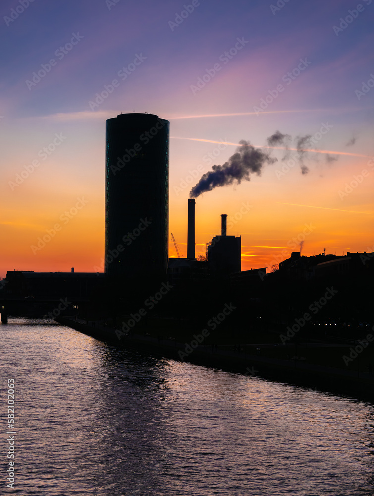 Silhouettes of a skyscraper and an industrial buildings along the banks of the Main River in Frankfurt, Germany at sunset