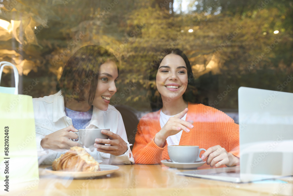 Special Promotion. Happy young women using laptop at table in cafe, view from outdoors Special Promotion. Happy young women using laptop at table in cafe, view from outdoors