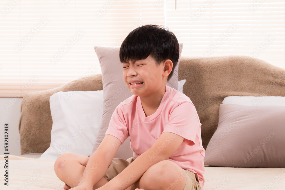 Asian adorable boy crying on bed because he didn't go out to play with his friends on holiday. young children making mistakenly crying in bedroom. son scolded by mother. Asian adorable boy crying on bed because he didn't go out to play with his friends on holiday. young children making mistakenly crying in bedroom. son scolded by mother.