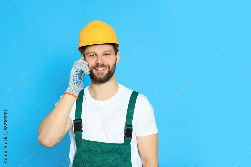 Professional repairman in uniform talking on smartphone against light blue background. Space for text Professional repairman in uniform talking on smartphone against light blue background. Space for text