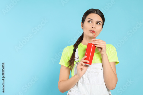 Beautiful happy woman drinking from red beverage can on light blue background. Space for text