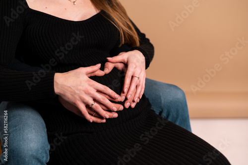 A husband and a pregnant wife together touch their tummy and make a heart with their hands