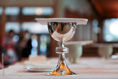 A shining silver communion chalice containing wine, a sacrament,  is covered with a chalice pall is resting on a table in an anglican church photo
