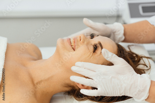 Woman beautician applies cream on face with massage. Care, relaxation, rejuvenation, nourishment of facial skin and smoothing wrinkles in cosmetology clinic. Girl on a spa procedure in a beauty salon