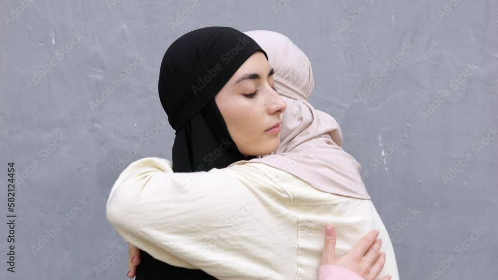 Two grieving Muslim women in black and white hijabs give each other