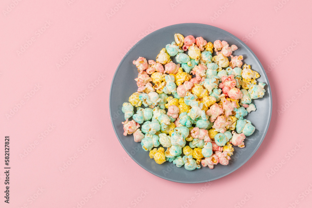 Multicolor sugary glazed popcorn on gray plate on a pink background top view