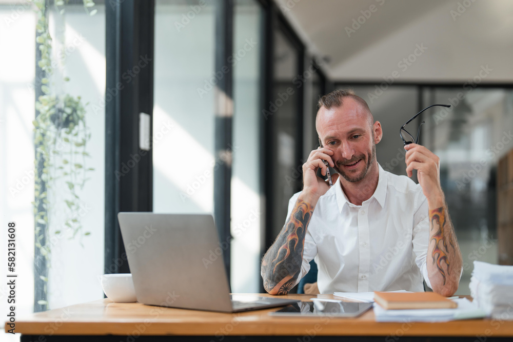 Accountant or bookkeeper using laptop computer while talking smartphone with accountant consult and for calculating tax, financial report Accountant or bookkeeper using laptop computer while talking smartphone with accountant consult and for calculating tax, financial report