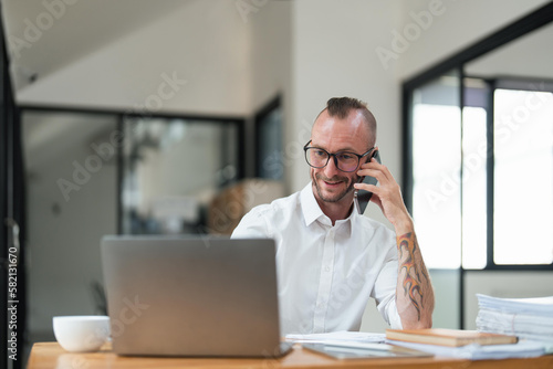 Accountant or bookkeeper using laptop computer while talking smartphone with accountant consult and for calculating tax, financial report