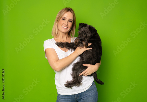 Portrait of attractive cheerful careful girl holding in hands doggy schnauzer isolated over bright green color background