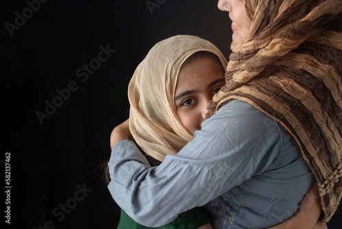 Closeup, Muslim Mother in traditional costume hugging her daughter on black background, family spending time together at home, girl looking at camera, Happy mother's day