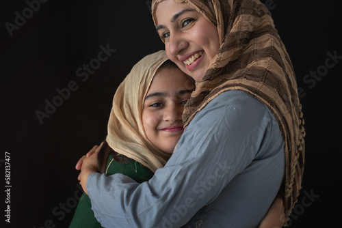 Closeup, Muslim Mother in traditional costume hugging her daughter on black background, family spending time together at home, Happy mother's day
