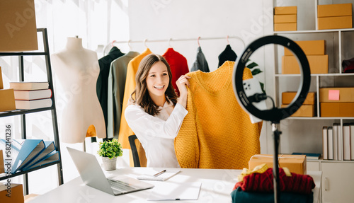 Fashion blogger concept, Young Asian women selling clothes on video streaming.Startup small business SME, using smartphone or tablet taking receive and checking