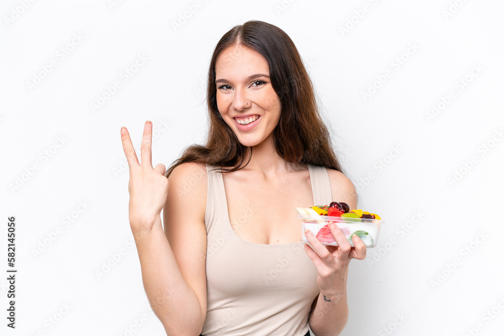 Young caucasian woman holding a bowl of fruit isolated on white background smiling and showing victory sign Young caucasian woman holding a bowl of fruit isolated on white background smiling and showing victory sign