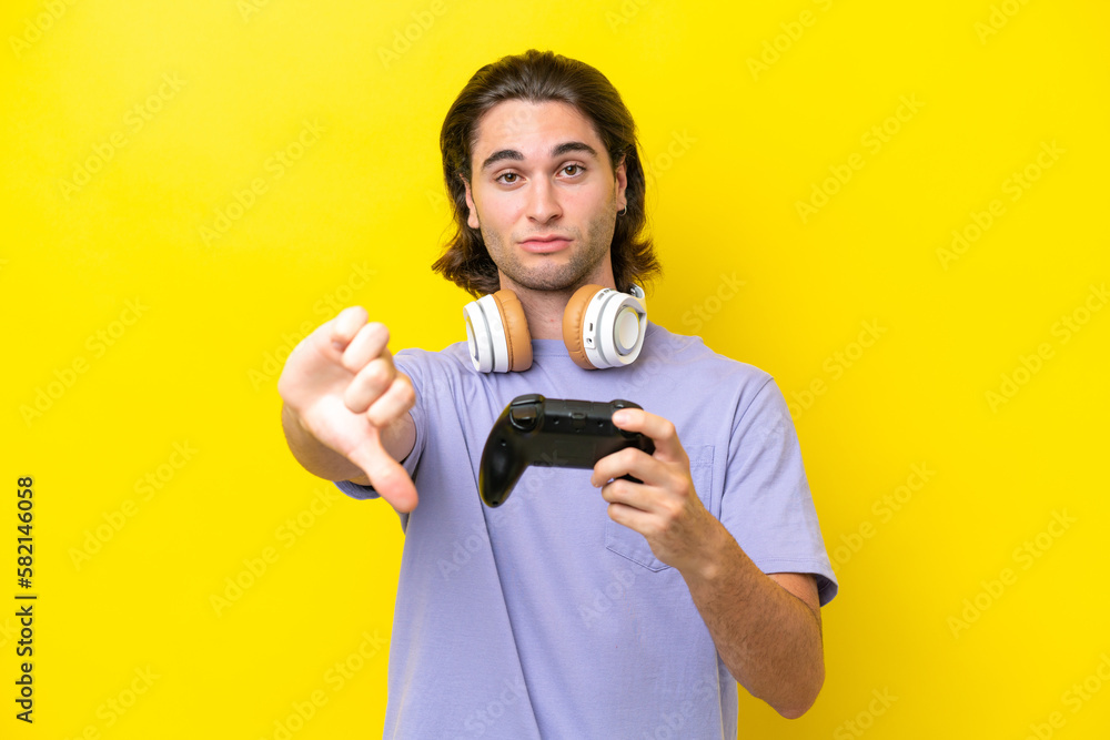 Young handsome caucasian man playing with a video game controller over isolated on yellow background showing thumb down with negative expression Young handsome caucasian man playing with a video game controller over isolated on yellow background showing thumb down with negative expression