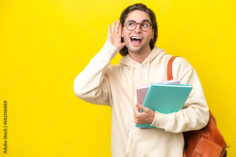 Young student handsome man isolated on yellow background listening to something by putting hand on the ear Young student handsome man isolated on yellow background listening to something by putting hand on the ear