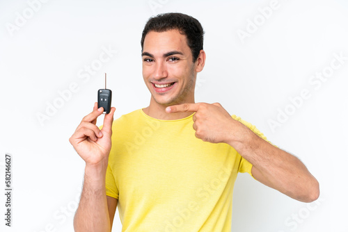 Young caucasian man holding car keys isolated on white background and pointing it