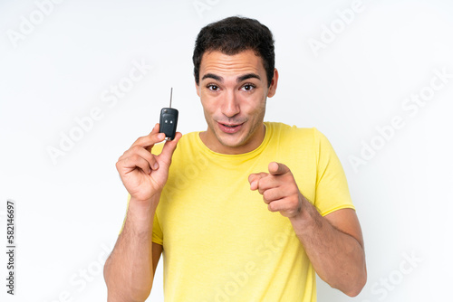 Young caucasian man holding car keys isolated on white background surprised and pointing front