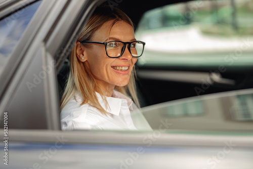 Portrait of attractive woman entrepreneur wearing glasses sit in city taxi and looking at window