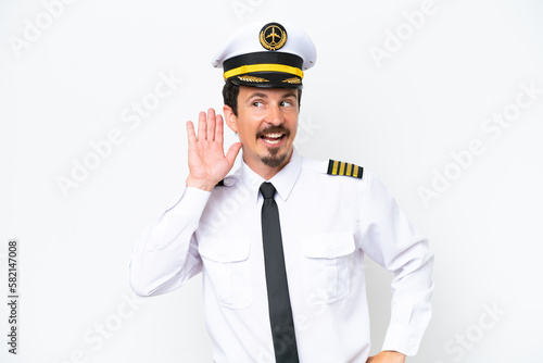 Airplane caucasian pilot isolated on white background listening to something by putting hand on the ear