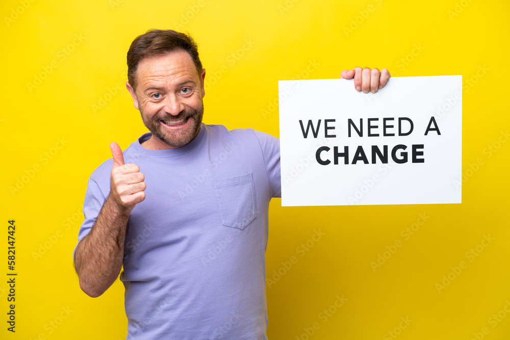 Middle age caucasian man isolated on yellow background holding a placard with text We Need a Change with thumb up Middle age caucasian man isolated on yellow background holding a placard with text We Need a Change with thumb up