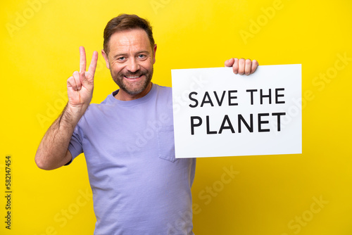 Middle age caucasian man isolated on yellow background holding a placard with text Save the Planet and celebrating a victory © luismolinero