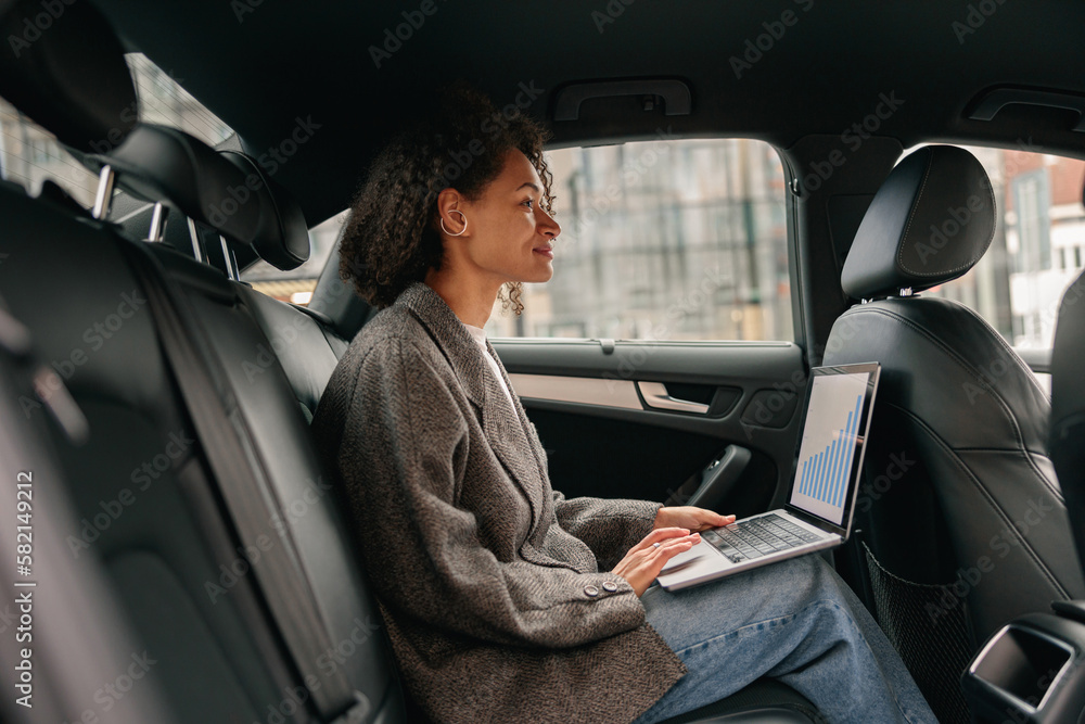 Executive woman sales manager working on laptop sitting car leather backseat on way to office