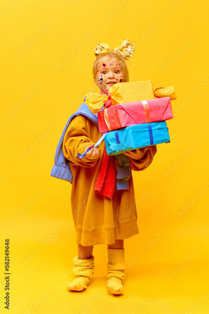 Full-length photo of little girl holding gifts, boxes with surprised face over yellow background. Concept of celebration, ad, children's products, childhood, child model, family Full-length photo of little girl holding gifts, boxes with surprised face over yellow background. Concept of celebration, ad, children's products, childhood, child model, family