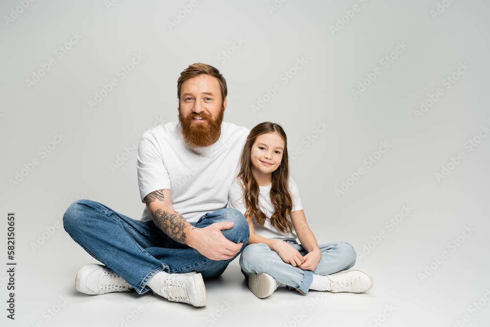 Carefree father and daughter in jeans and t-shirts sitting on grey background. Carefree father and daughter in jeans and t-shirts sitting on grey background.