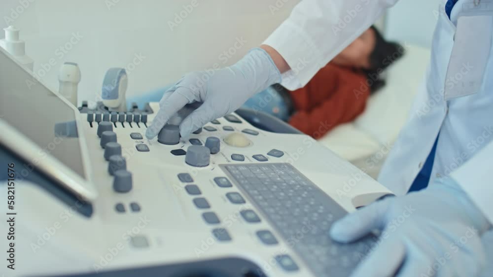 Selective focus medium close-up of unrecognizable medical worker setting medical ultrasound scanner for patient Selective focus medium close-up of unrecognizable medical worker setting medical ultrasound scanner for patient