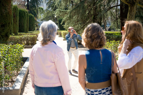 group of middle-aged friends pose in the park while a friend takes pictures of them © luisrojasstock