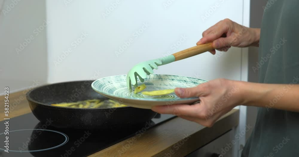 Woman getting hot french fries from pan on the plate Woman getting hot french fries from pan on the plate
