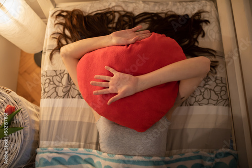 The red heart-shaped pillow is lying on the girls face. photo