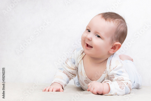 Kid with a smile on a white background. An adorable six month old baby boy is lying on the bed. Conceptual photo of fatherhood and motherhood.