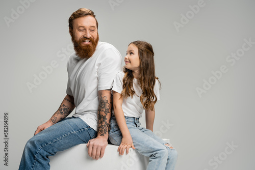 Positive man and child sitting back to back on cube isolated on grey.